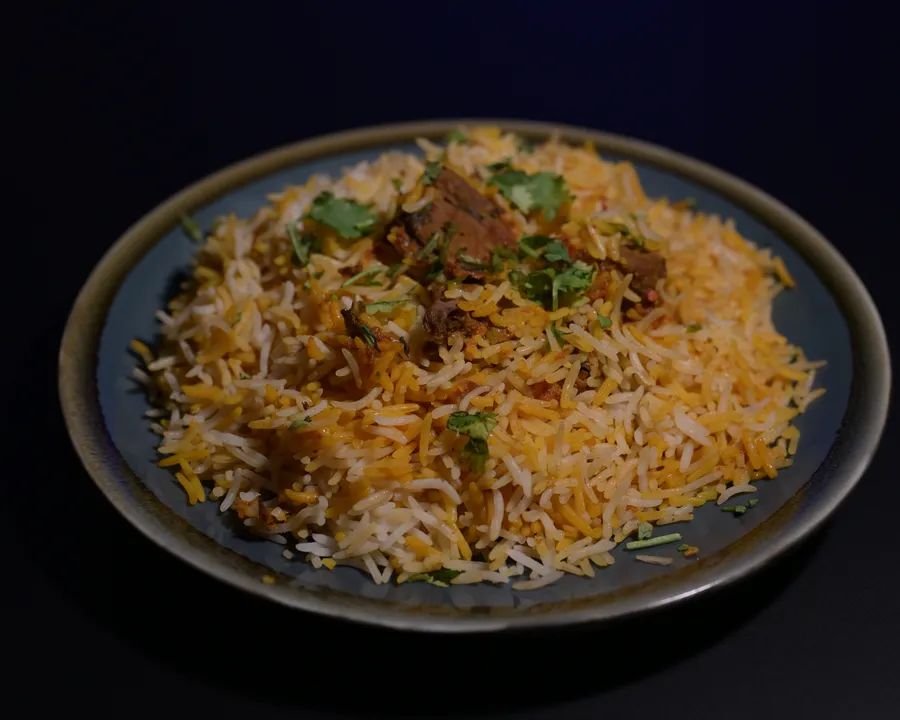 Biryani of layered saffron basmati, tender beef and fresh coriander on a dark plate