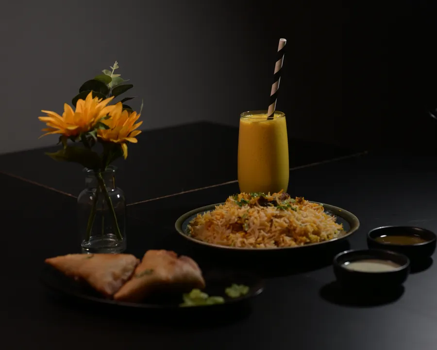 Mango mocktail with a striped straw, served beside biryani and samosas