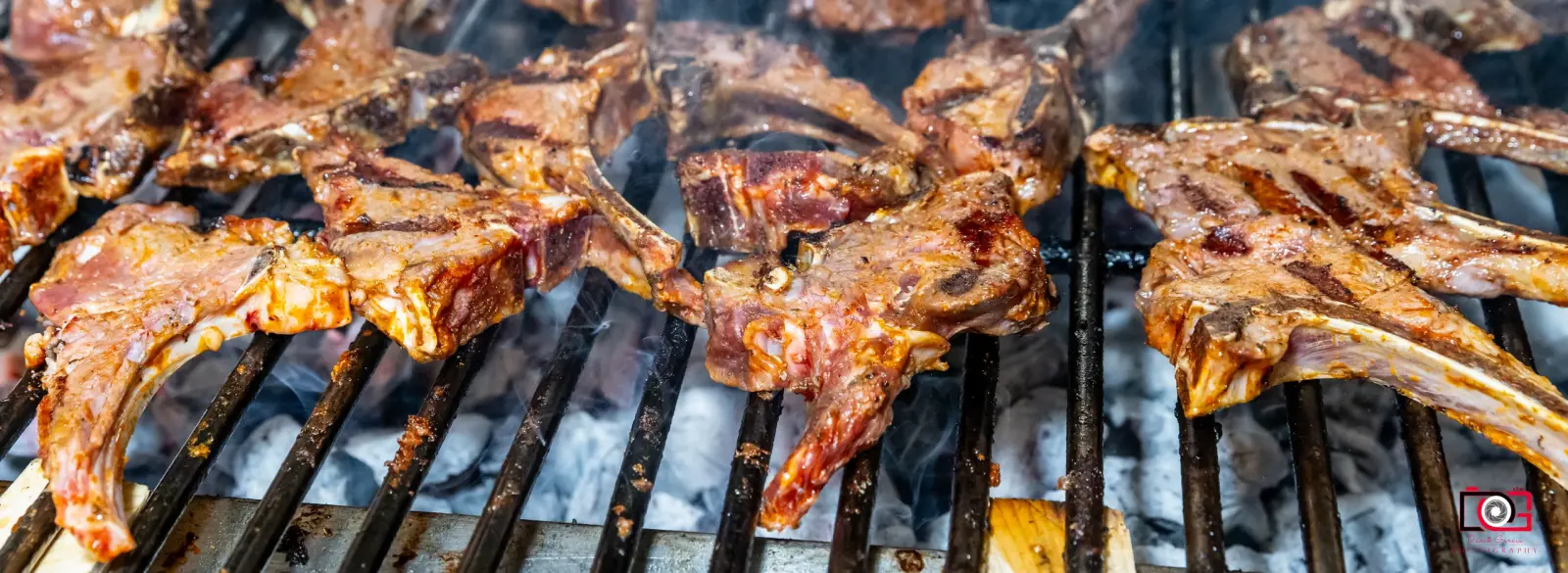 A wide view across the charcoal grill, lamb chops resting over glowing coals