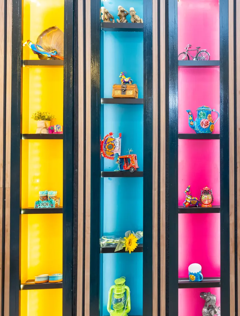 Display shelving in marigold, turquoise and pink holding painted folk objects