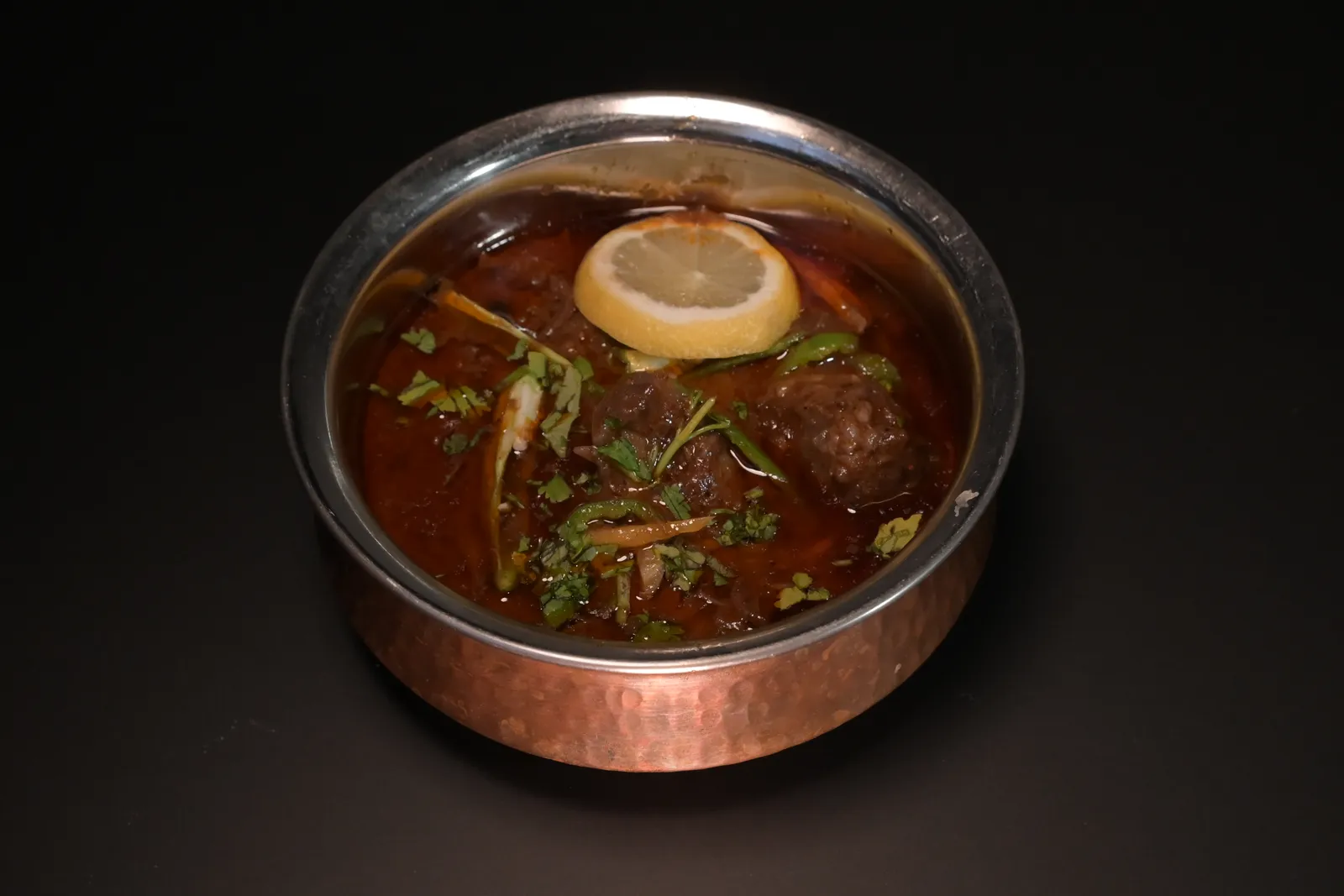 Beef nihari in a copper karahi, garnished with lemon, ginger and coriander